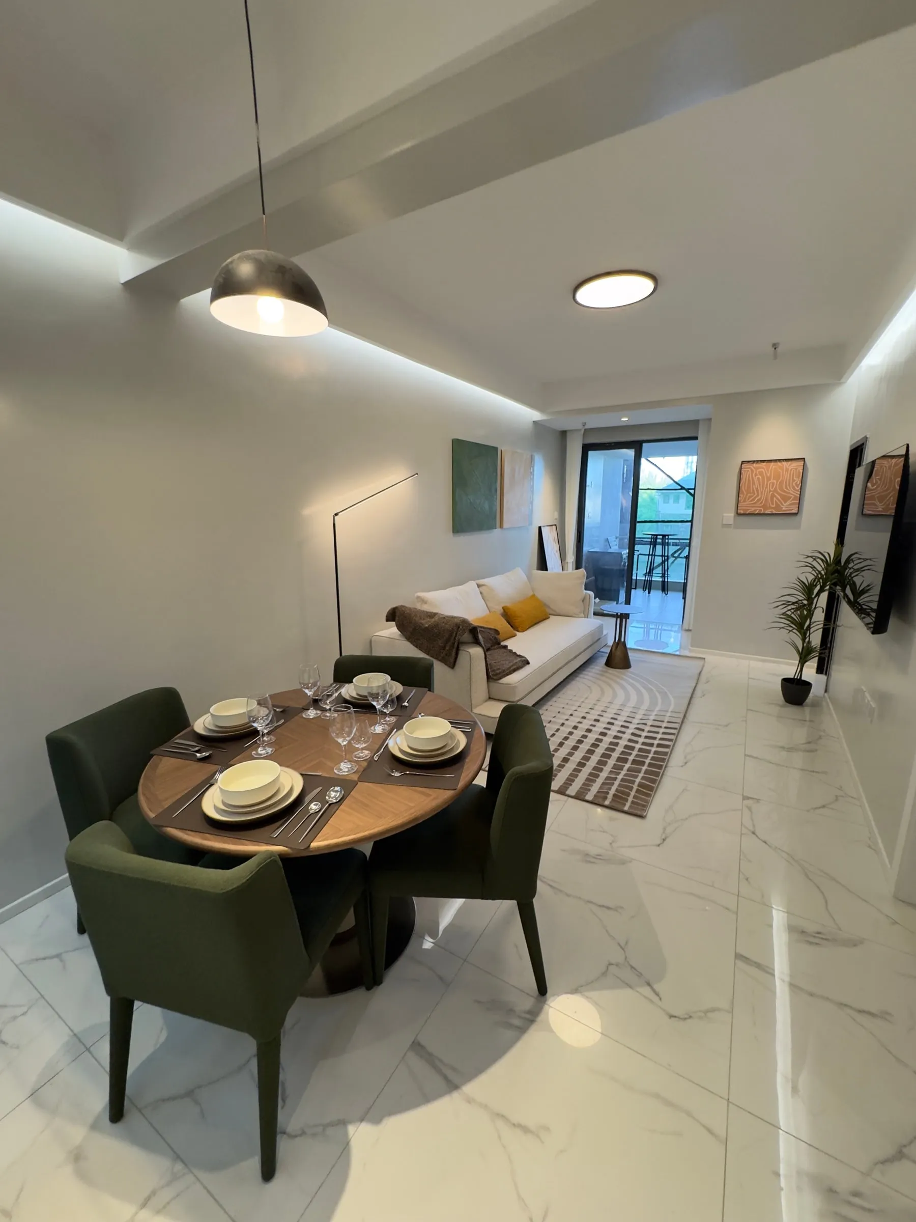 Round dining table with green chairs, sofa and balcony door behind